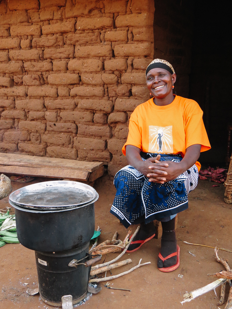 Moshi shows off her high-efficiency wood burning cookstove. She is cooking a pot full of sweet potatoes and plantains which we shared with her family for dinner.