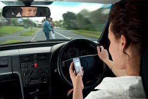 This photo shows a woman driving and texting, who is about to hit a mother and child crossing the street. 
