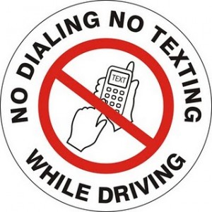 This photo shows a red line through a hand texting on a cell phone. The words "No Dialing, No Dialing While Driving" circle around the hand.