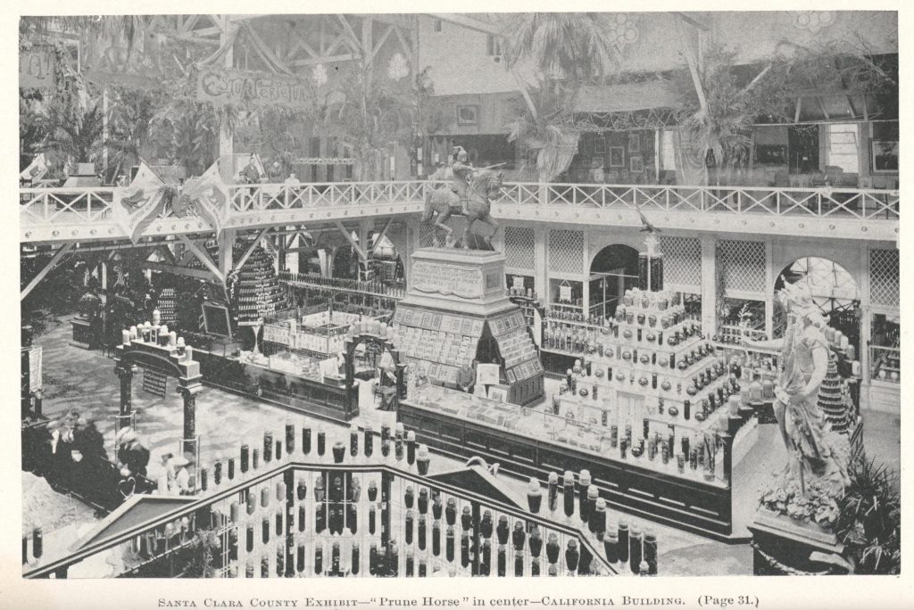 a statue of a man on a horse (the prune horse) stands atop a container of prunes and is surrounded by various goods from santa clara county: California Republic flags are seen hung as well as many, many jars filled with fruits