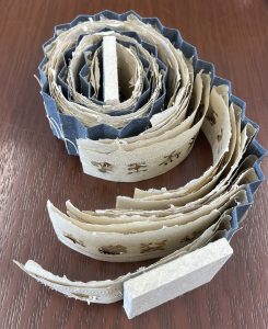 A spiral book with crinkled edges and symbols cut out of the pages.