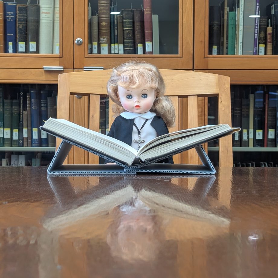Doll in a habit with a book on a support in the reading room.