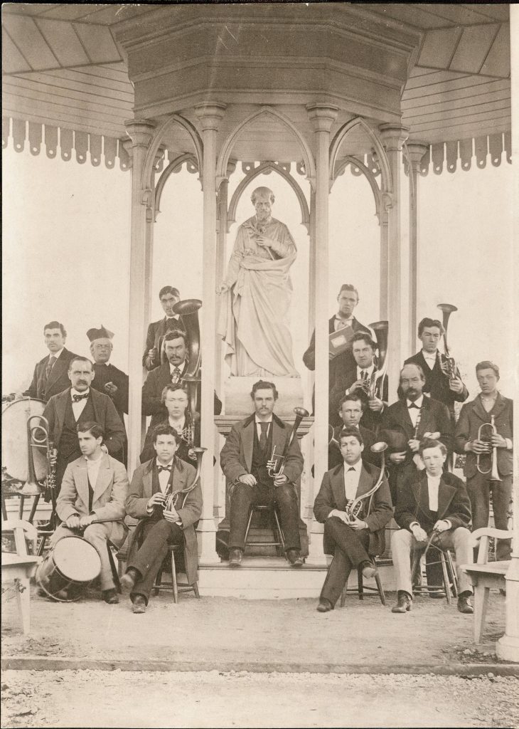 Young men with musical instruments in suits sitting in a gazebo with a statue of St. Joseph.
