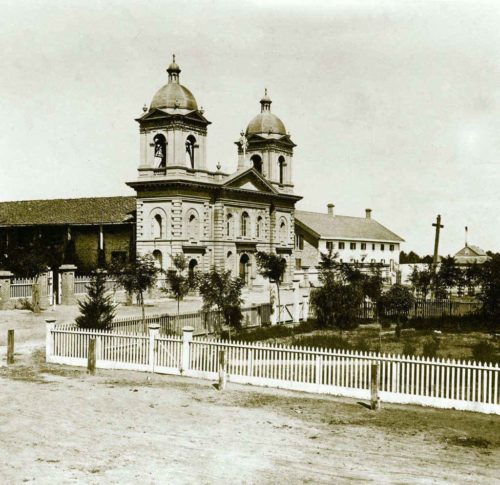 Mission Church with an Italianate facade adn a white picket fence enclosing gardens