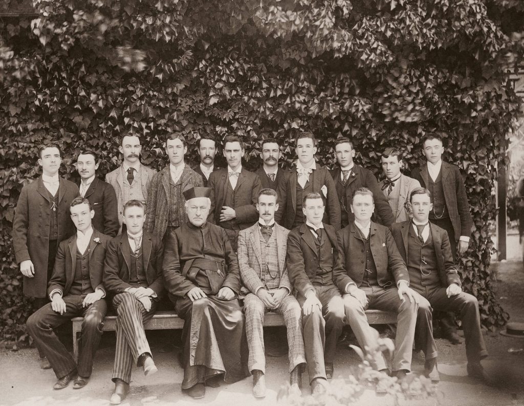 Young men in suits with a Jesuit outdoors
