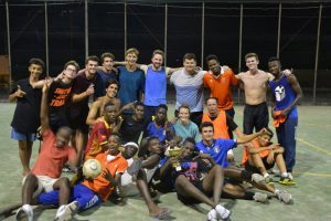 Group of American abroad students and adolescent African migrants on a concrete soccer court